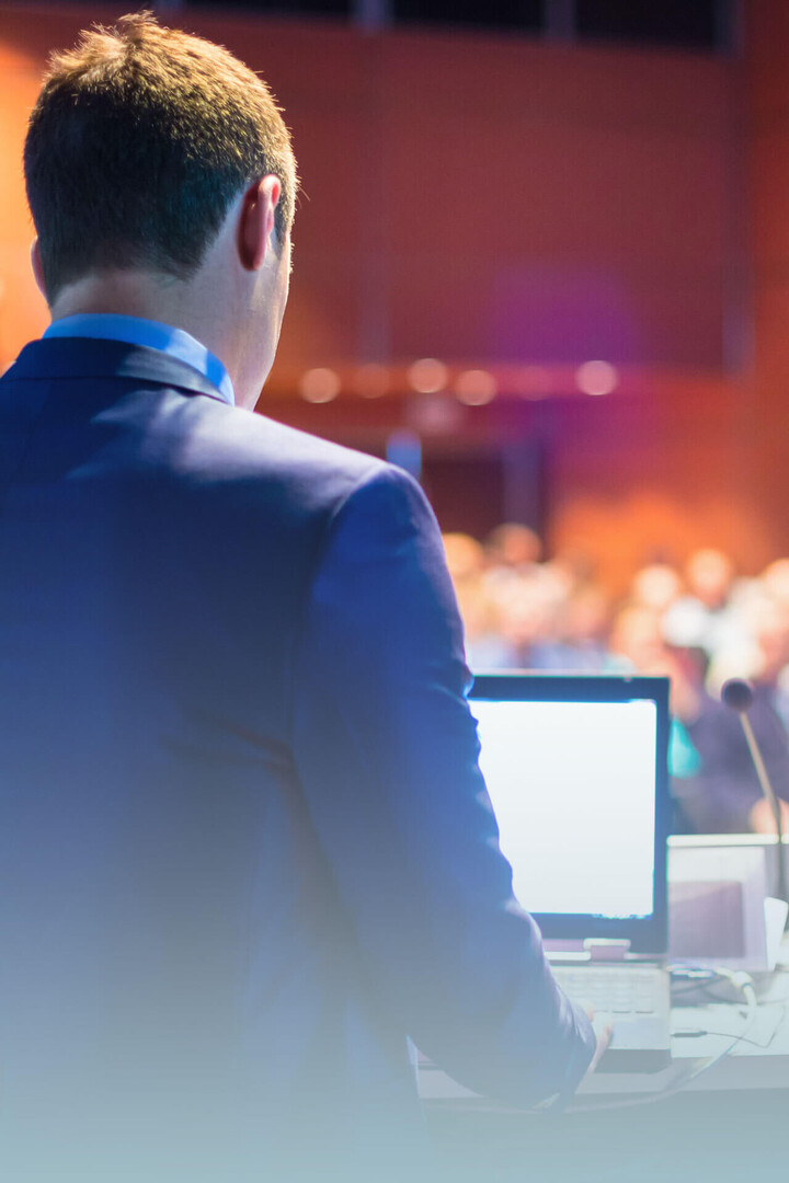 Mann spricht bei einer Konferenz am Rednerpult mit Laptop